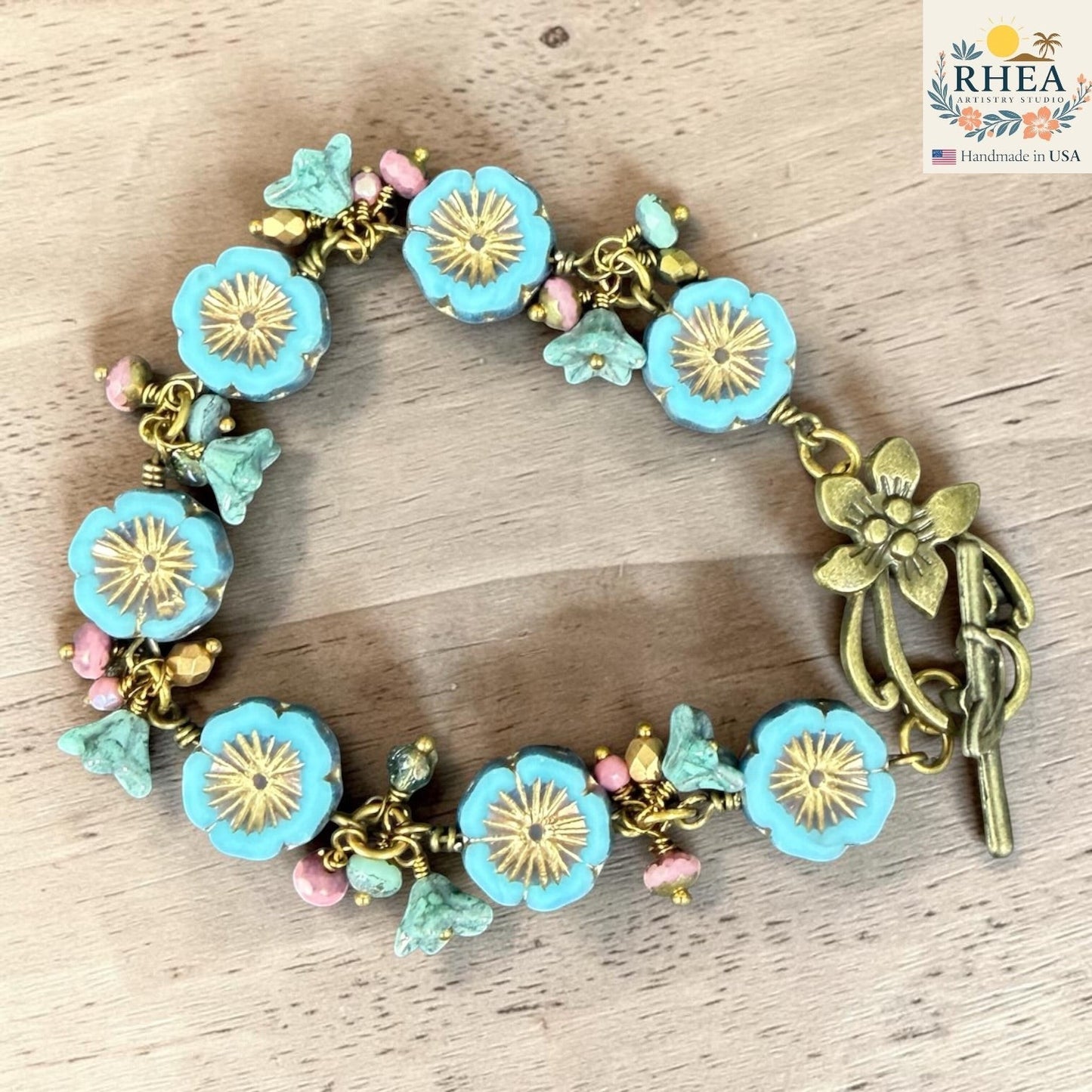 Rhea Artistry Studio handmade bracelet with blue glass flower beads, pink accent beads, and antique brass toggle clasp.