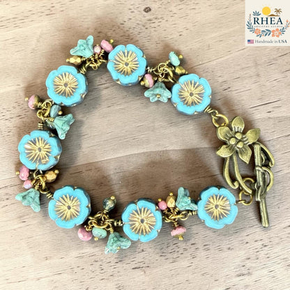 Rhea Artistry Studio handmade bracelet with blue glass flower beads, pink accent beads, and antique brass toggle clasp.