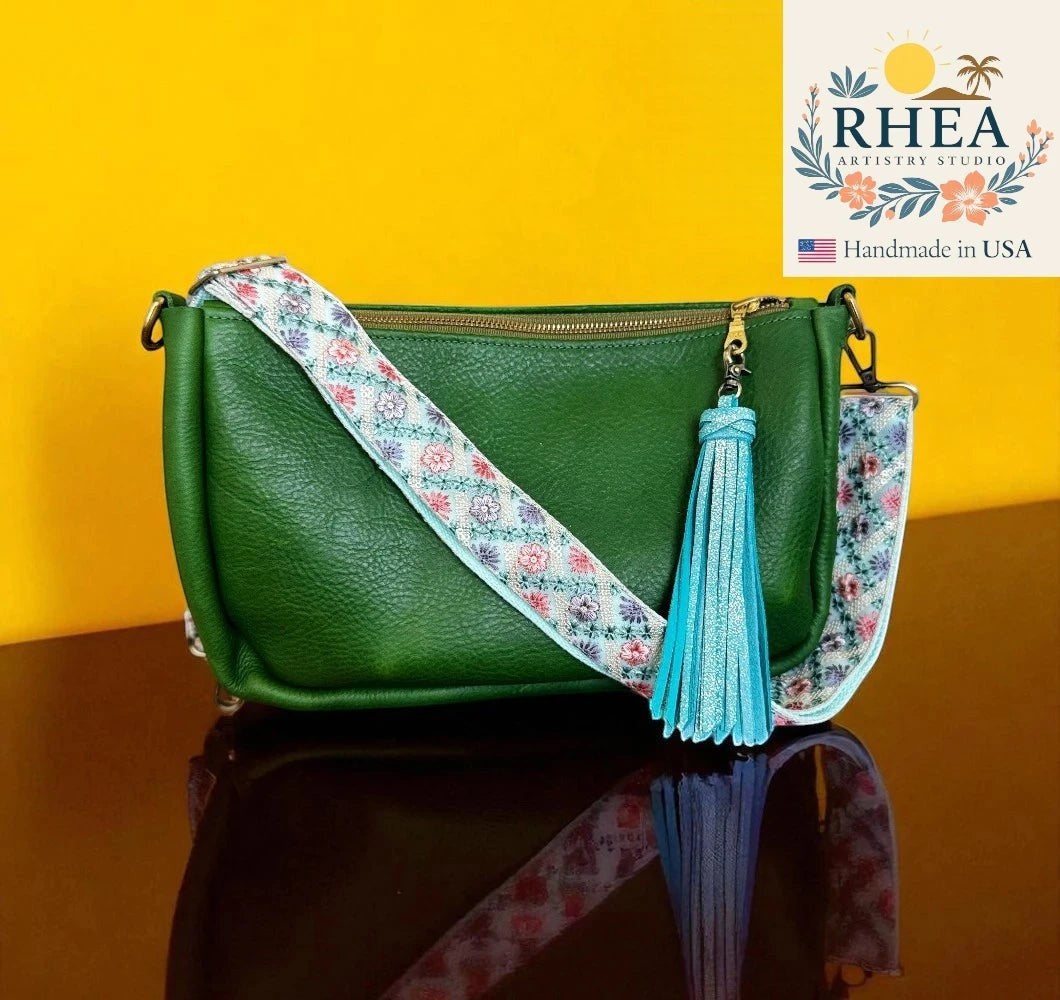 Rhea Artistry Studio blue floral embroidered crossbody strap with blue tassel on a green leather bag.
