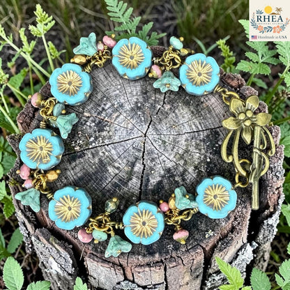 Rhea Artistry Studio handmade bracelet with blue glass flower beads, pink accent beads, and antique brass hardware.