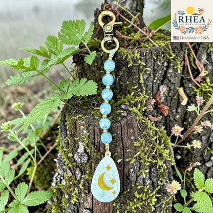 Rhea Artistry Studio blue multi-faceted glass bead bag charm with moon and stars pendant and brass hardware.