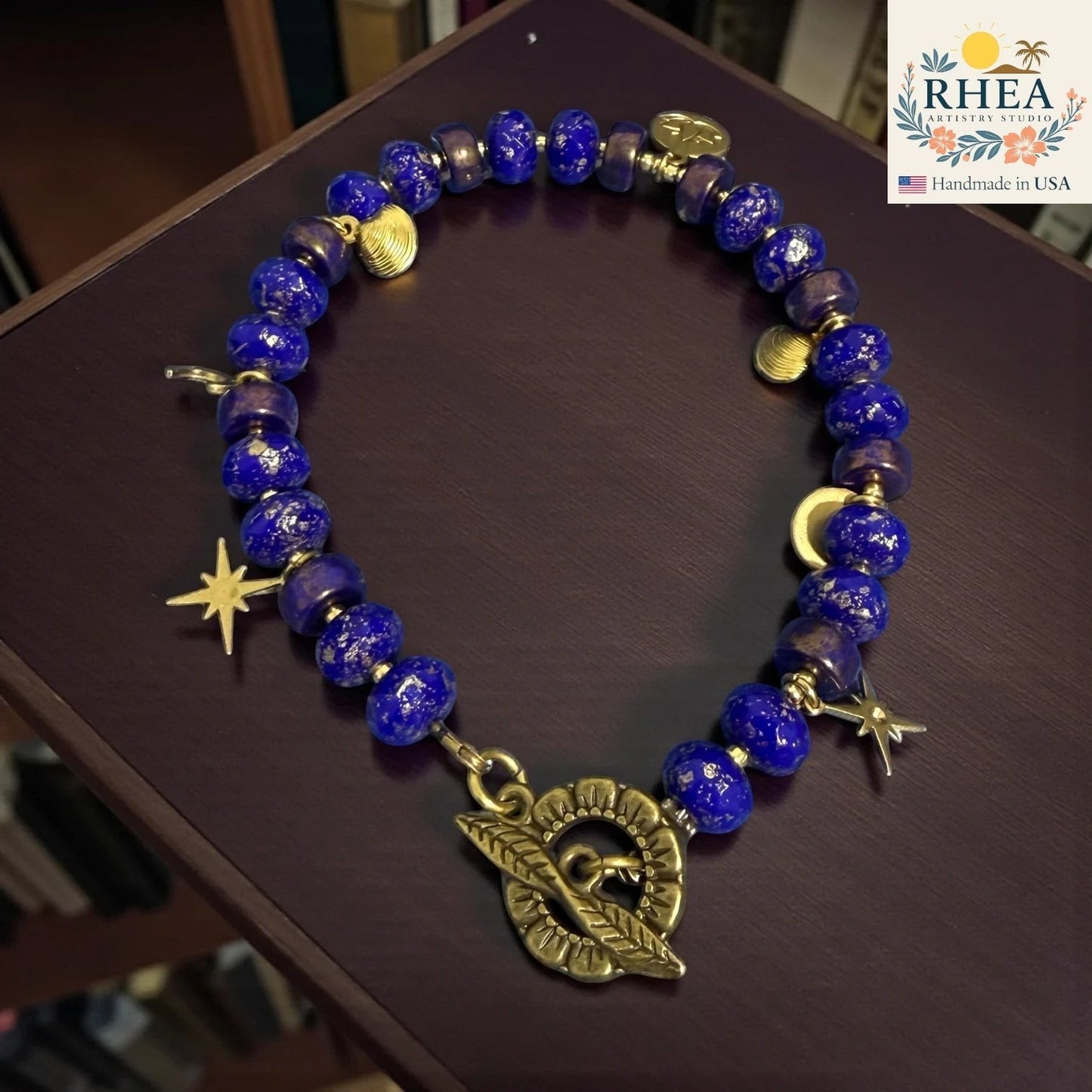 Rhea Artistry Studio handmade celestial bracelet with deep blue glass beads, brass star and moon charms, and floral toggle clasp.