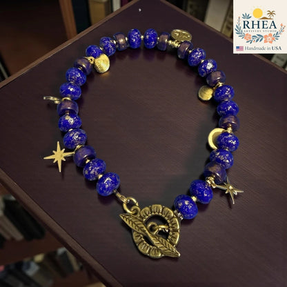 Rhea Artistry Studio handmade celestial bracelet with deep blue glass beads, brass star and moon charms, and floral toggle clasp.