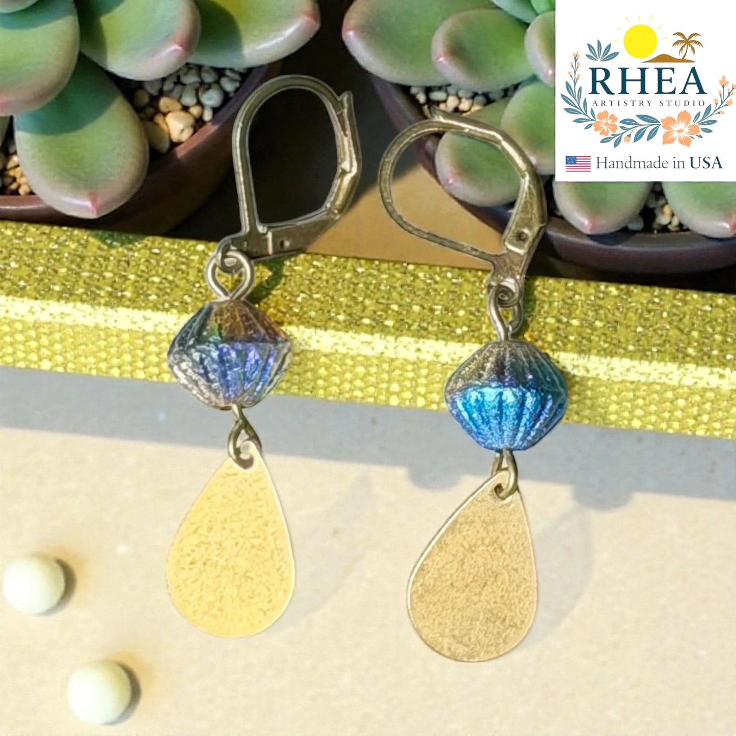 Rhea Artistry Studio handcrafted drop earrings with faceted blue glass beads and brushed brass teardrop charms, 2 inches long.