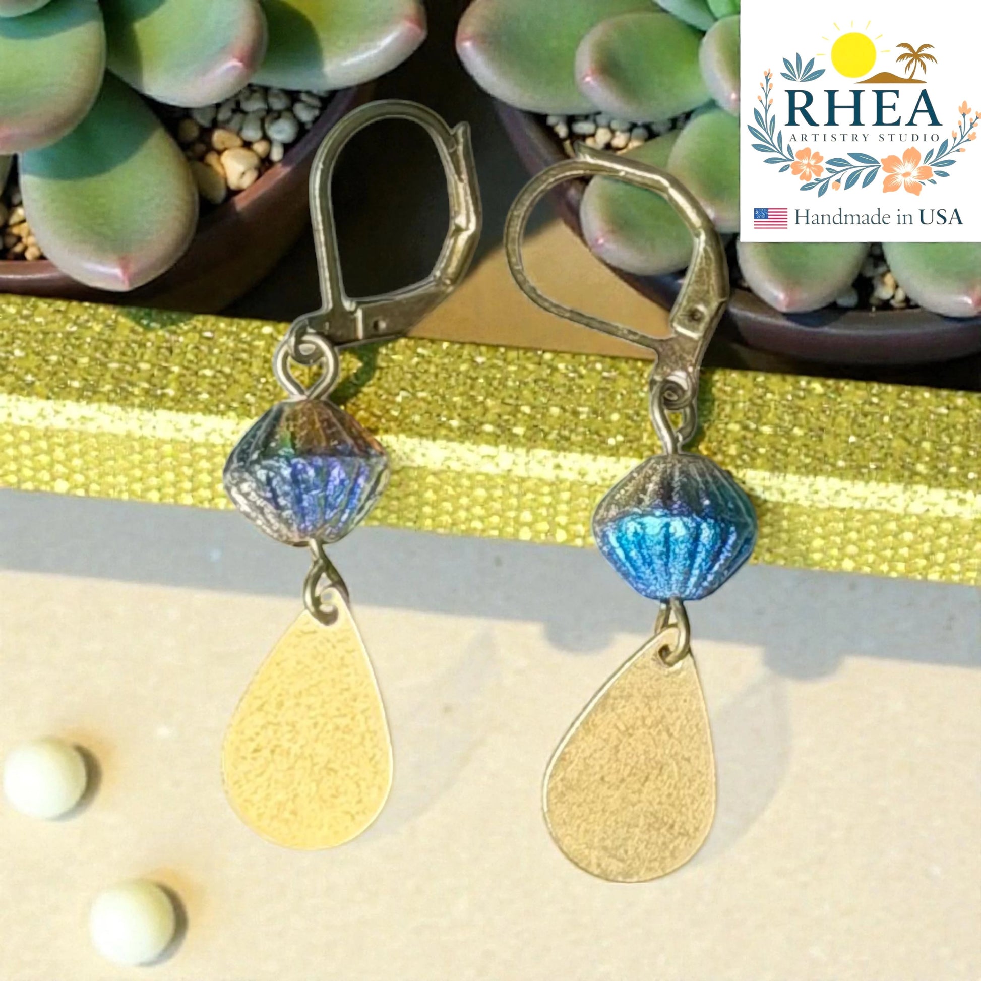 Rhea Artistry Studio handcrafted drop earrings with faceted blue glass beads and brushed brass teardrop charms, 2 inches long.