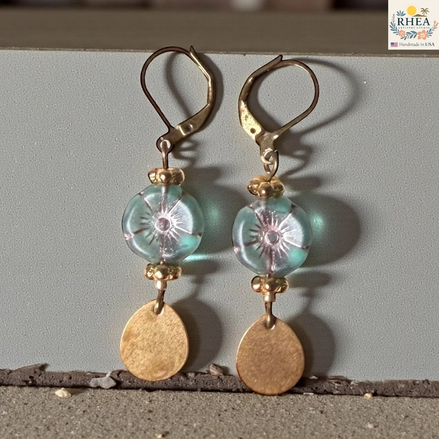 Rhea Artistry Studio light blue glass hibiscus flower drop earrings with gold-tone brass hardware and leverback hooks.