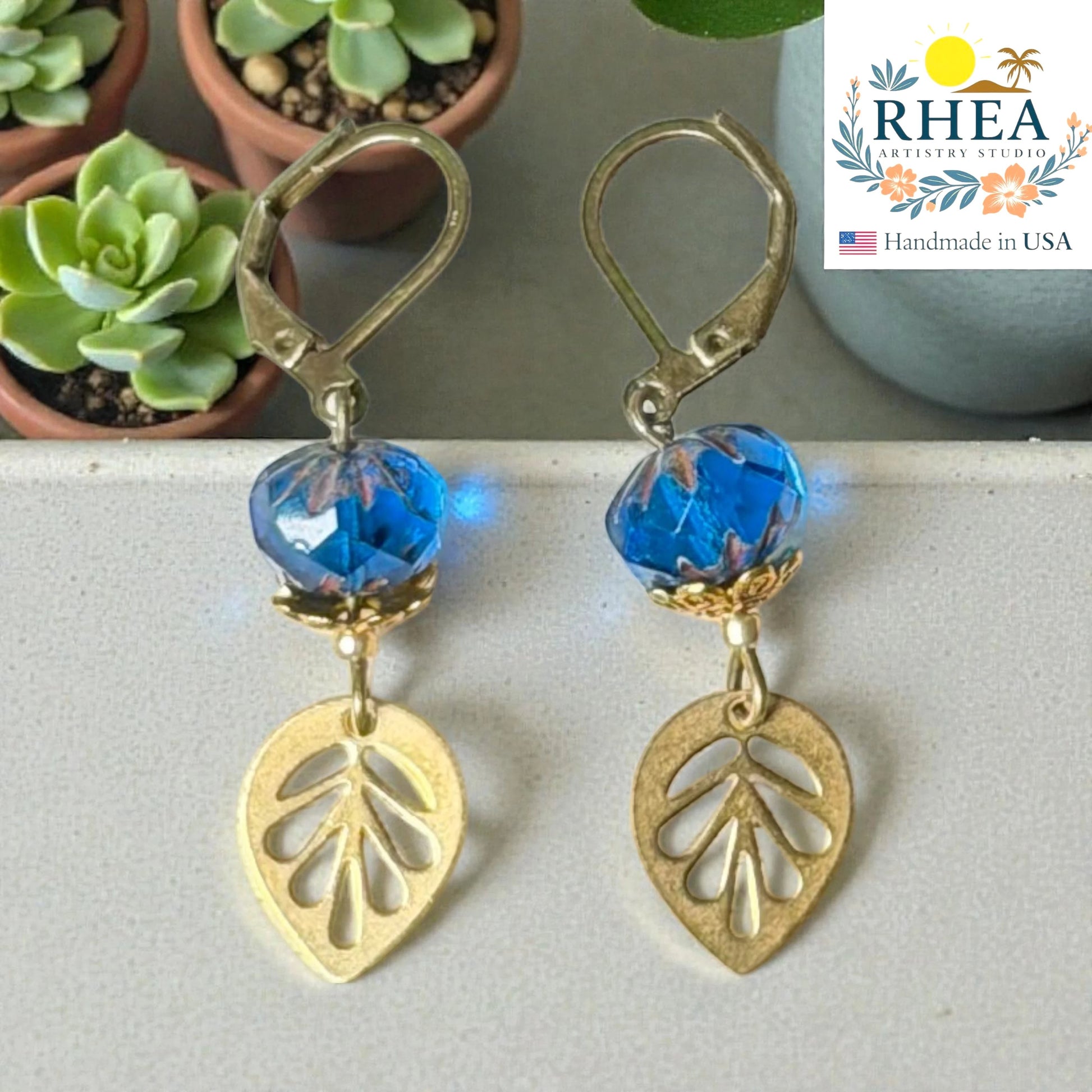 Rhea Artistry Studio blue faceted glass bead and brass leaf drop earrings, approx. 2 inches long, with leverback closures.