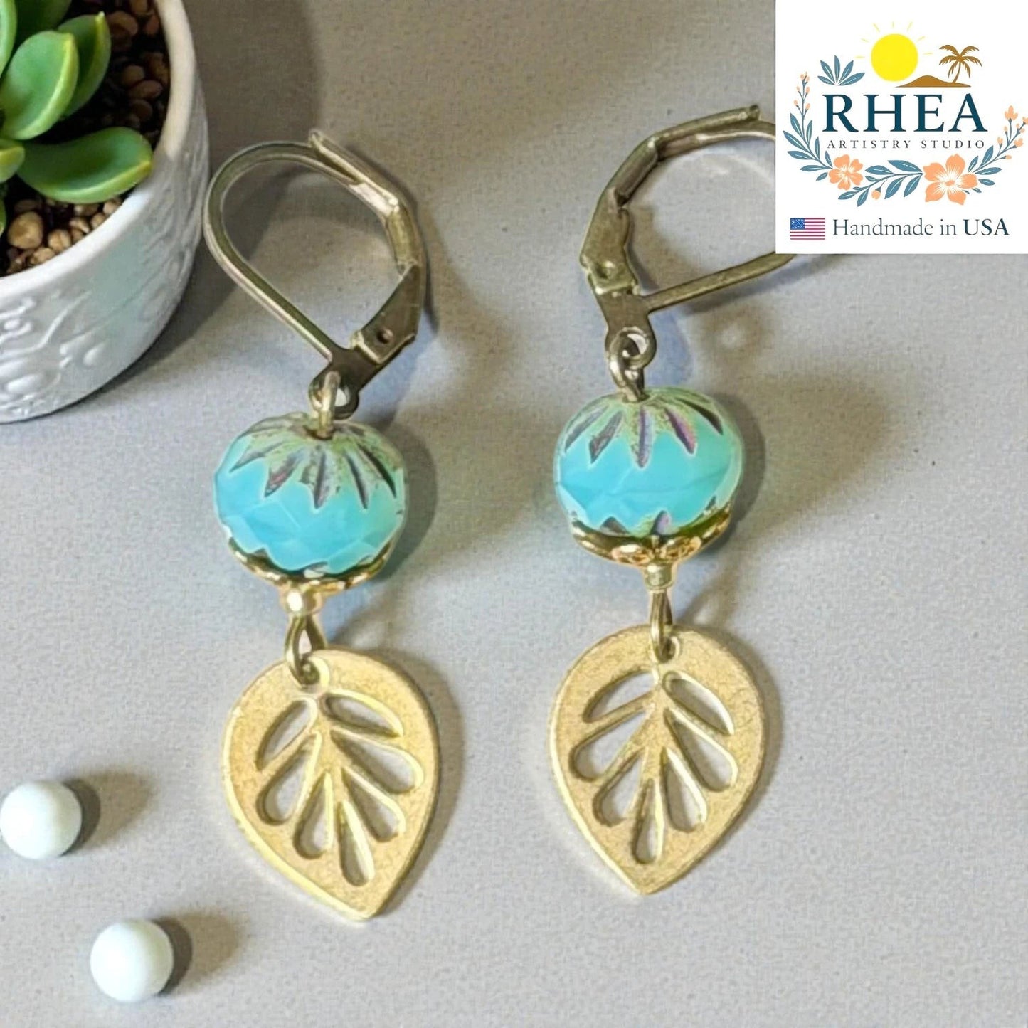 Rhea Artistry Studio blue faceted glass bead and brass leaf drop earrings, approx. 2 inches long, with leverback closures.