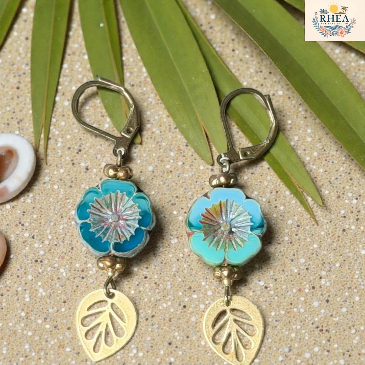 Rhea Artistry Studio blue and teal hibiscus glass drop earrings with gold leaf charms and lever back hooks.