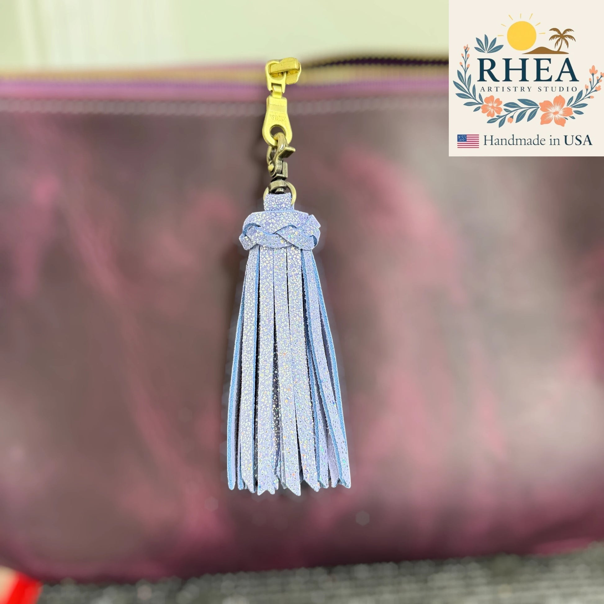 Rhea Artistry Studio handmade light blue leather tassel keychain with glitter detail and antique brass lobster clasp attached to a purple bag.