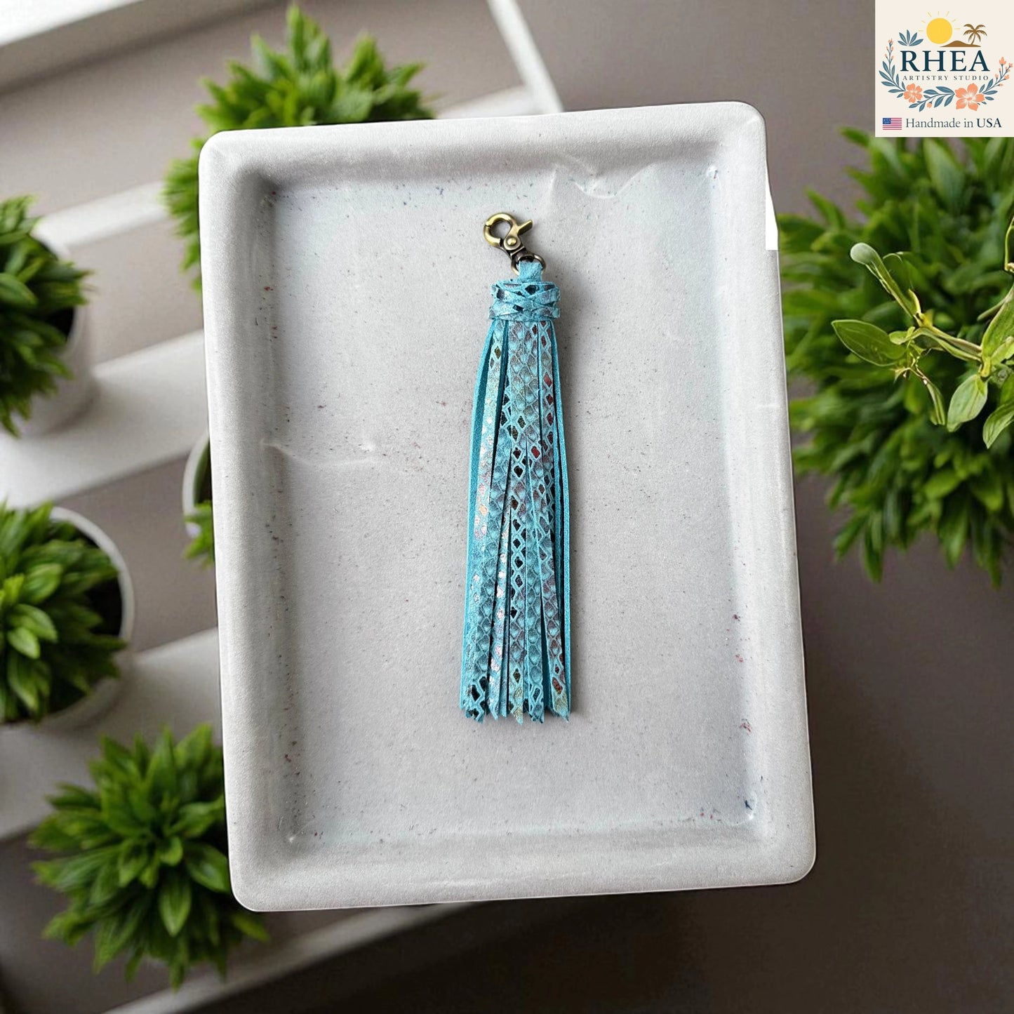 Rhea Artistry Studio handmade light blue leather tassel keychain with glitter accents and antique brass lobster clasp.