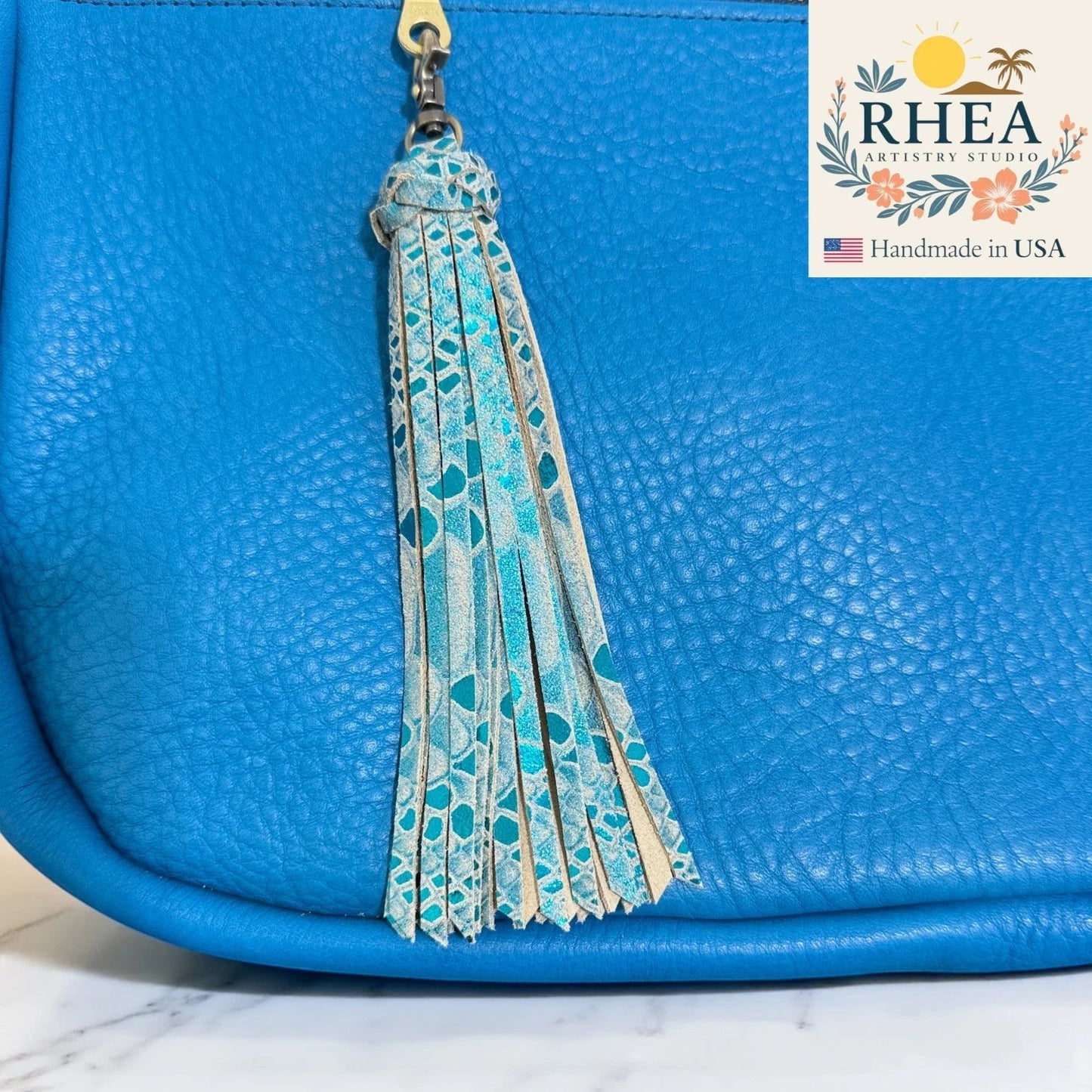 Rhea Artistry Studio handmade blue leather tassel keychain with turquoise pattern and lobster clasp on a blue bag.