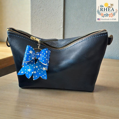 Rhea Artistry Studio blue double-layer French bow charm with white stars and holographic finish, attached to a black leather bag.