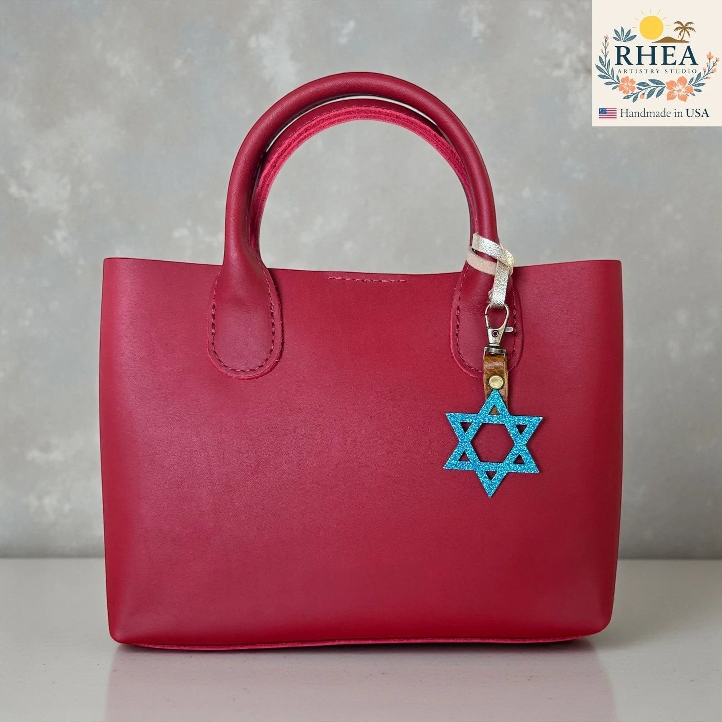 Rhea Artistry Studio blue glitter Star of David charm attached to a red leather handbag.