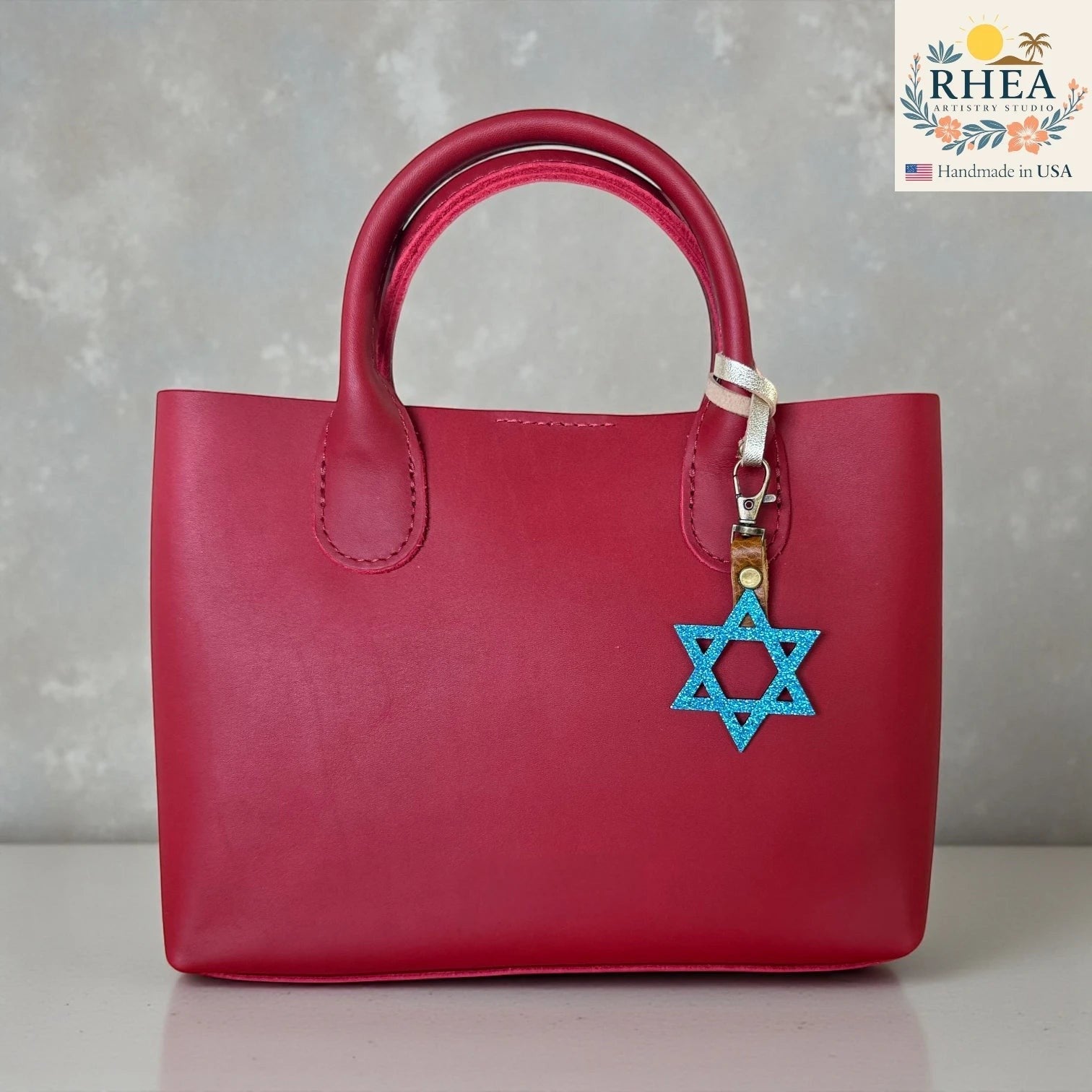 Rhea Artistry Studio blue glitter Star of David charm attached to a red leather handbag.