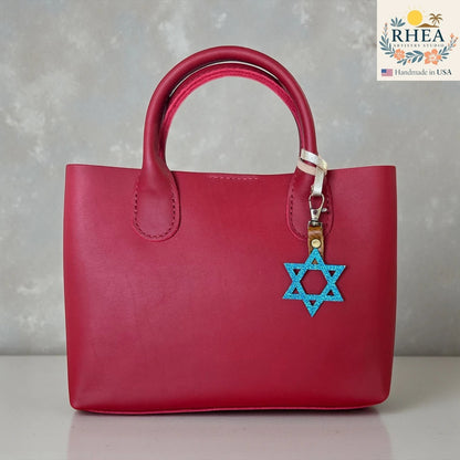 Rhea Artistry Studio blue glitter Star of David charm attached to a red leather handbag.