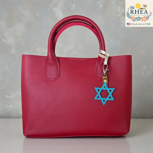 Rhea Artistry Studio blue glitter Star of David charm attached to a red leather handbag.