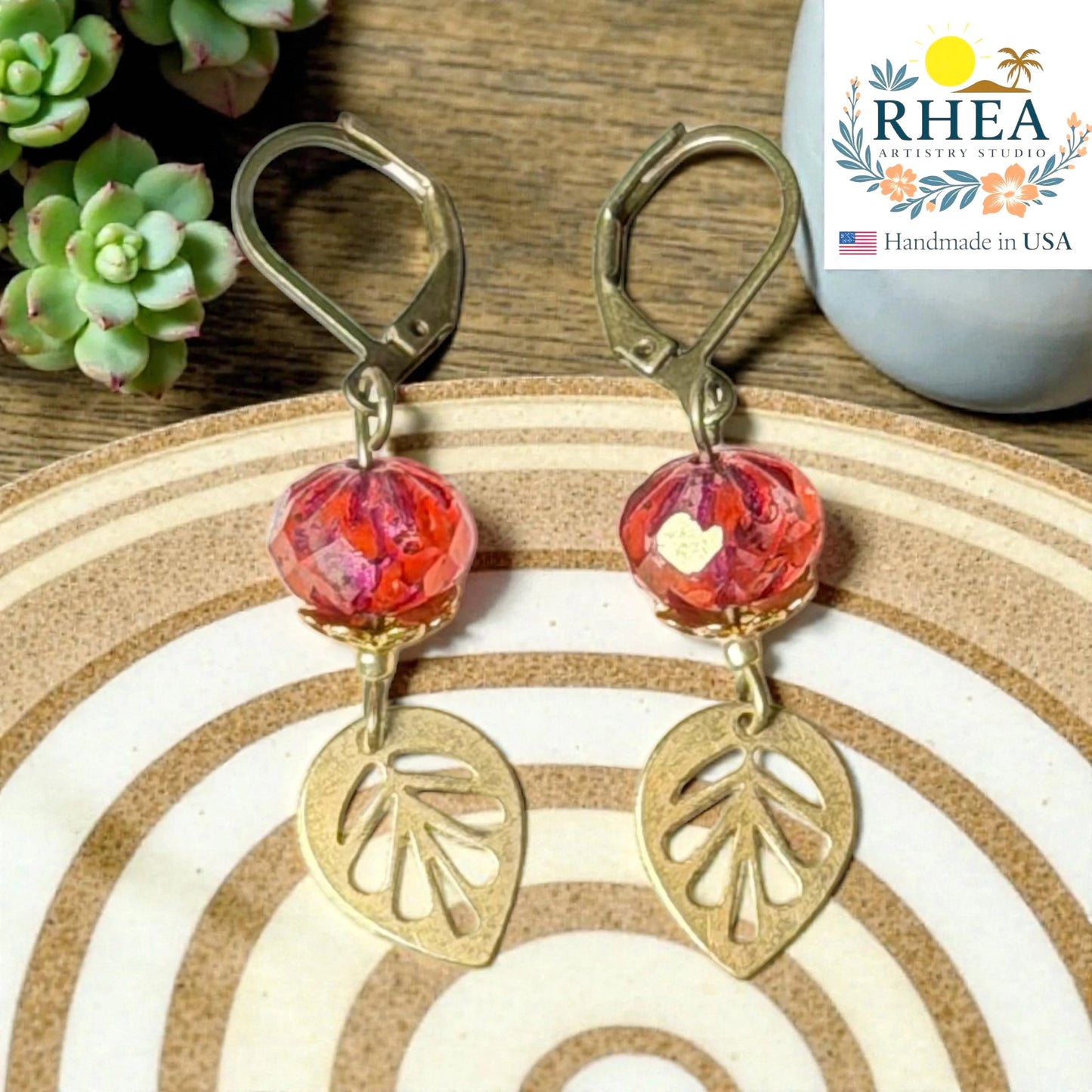 Rhea Artistry Studio handcrafted brass leaf drop earrings with faceted red glass beads and leverback closures.