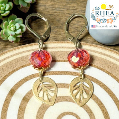 Rhea Artistry Studio handcrafted brass leaf drop earrings with faceted red glass beads and leverback closures.
