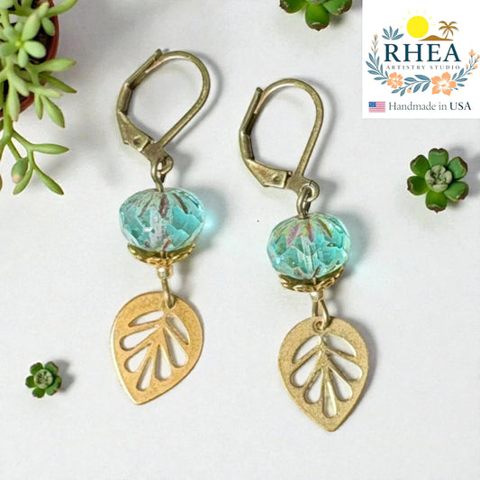 Rhea Artistry Studio handcrafted brass leaf drop earrings with faceted aqua glass beads, 2 inches long.