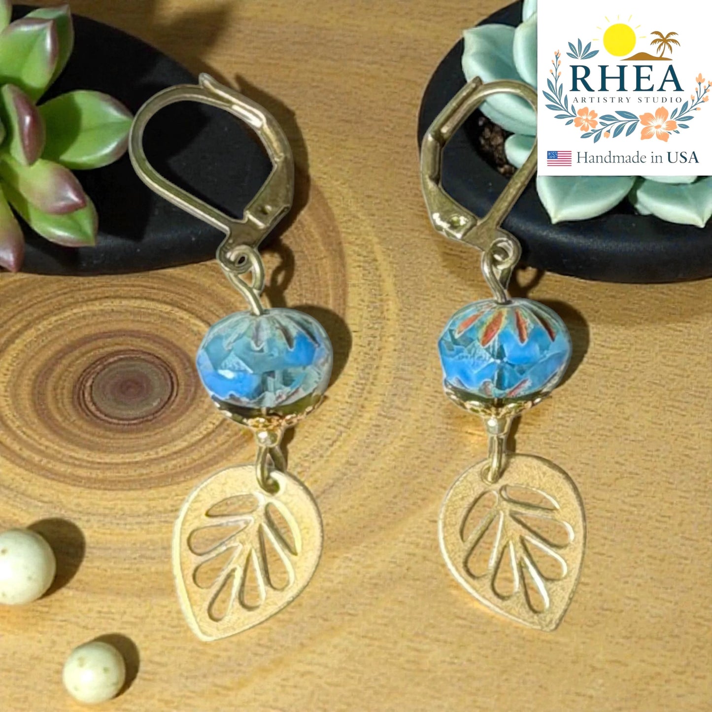 Rhea Artistry Studio blue faceted glass bead and brass leaf drop earrings, approx. 2 inches long, with leverback closures.
