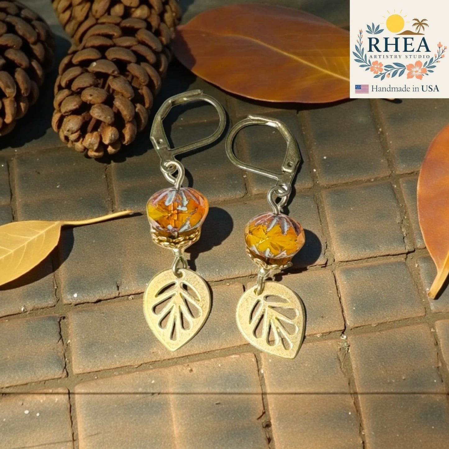 Rhea Artistry Studio handcrafted brass leaf drop earrings with faceted orange glass beads, 2 inches long, leverback closure.