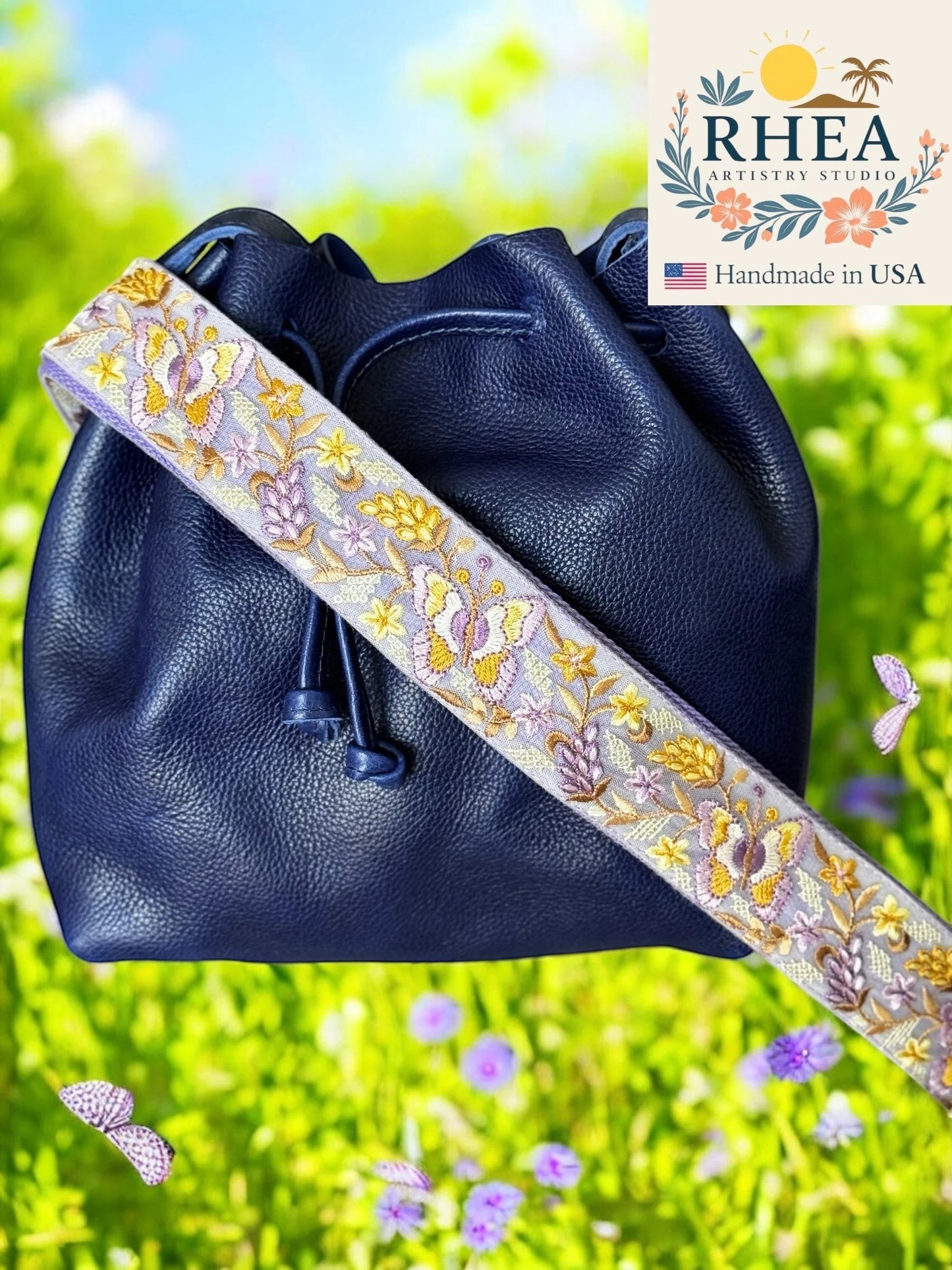 Rhea Artistry Studio 2-inch wide crossbody strap with purple, yellow, and white floral and butterfly embroidery on a light grey background.