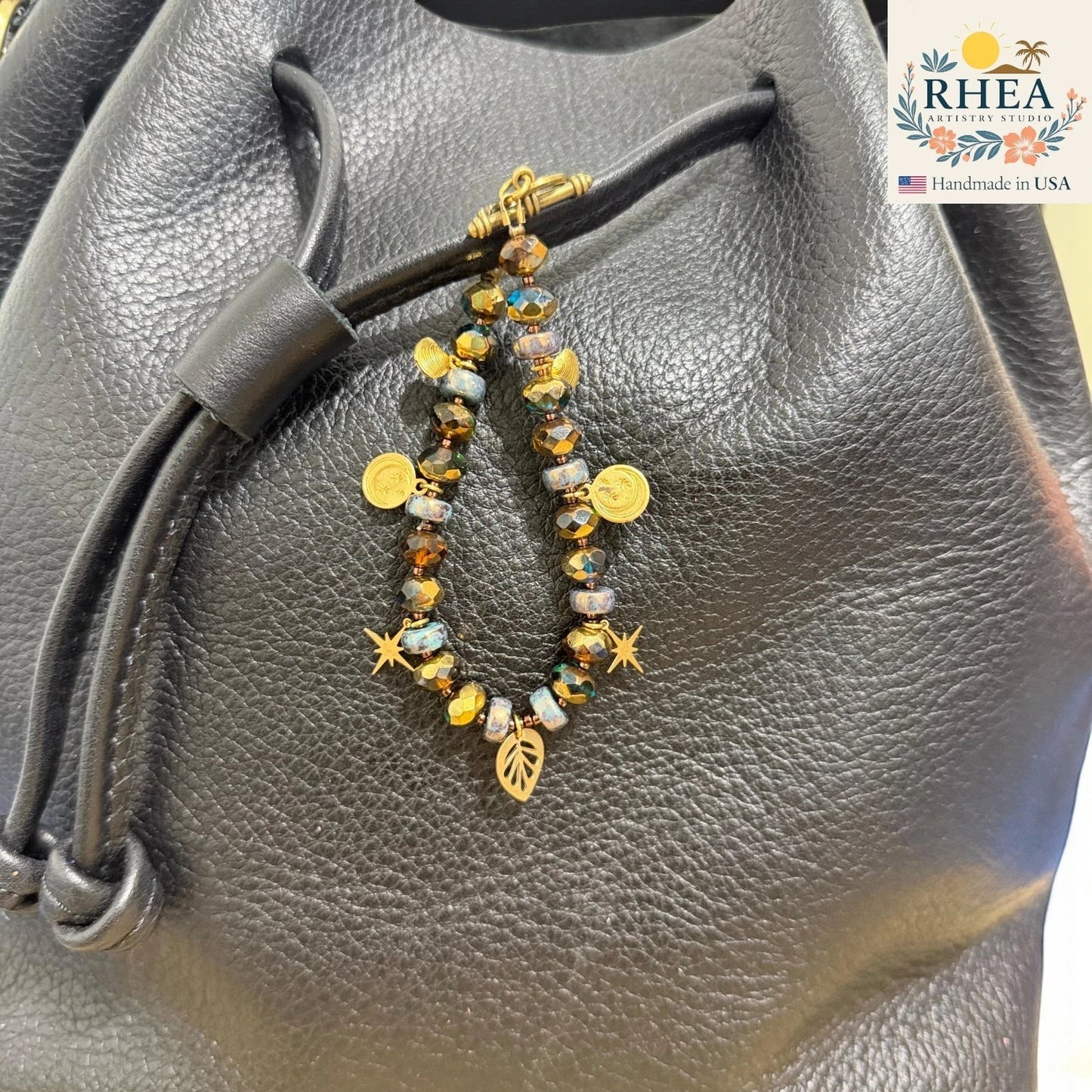 Rhea Artistry Studio handmade beaded purse charm with brass celestial charms, stars, leaf, and moons on a black leather bag.