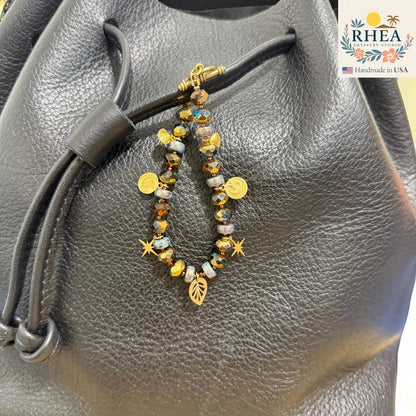 Rhea Artistry Studio handmade beaded purse charm with brass celestial charms, stars, leaf, and moons on a black leather bag.