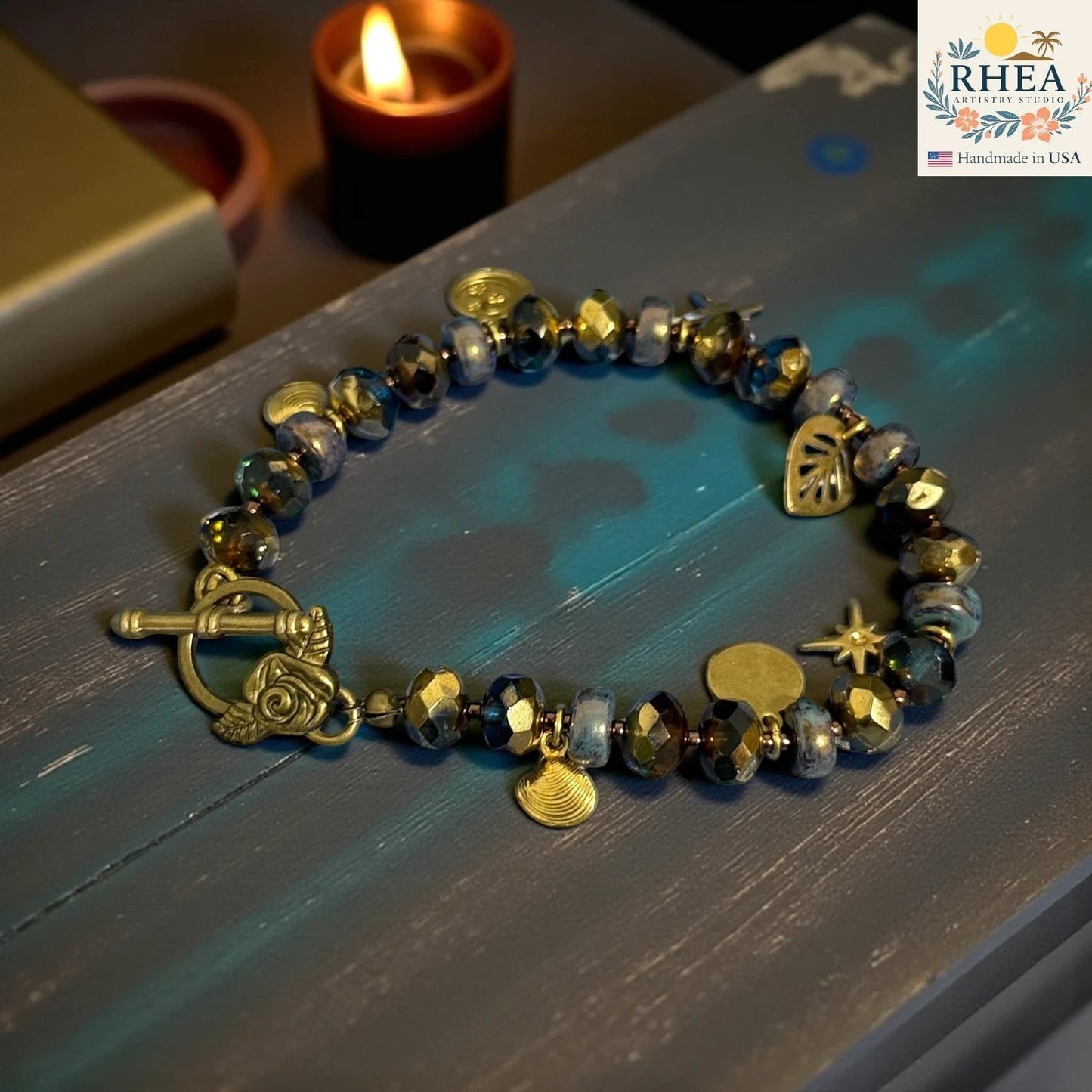 Rhea Artistry Studio handmade bracelet with blue and gold glass beads, celestial charms, and floral toggle clasp.