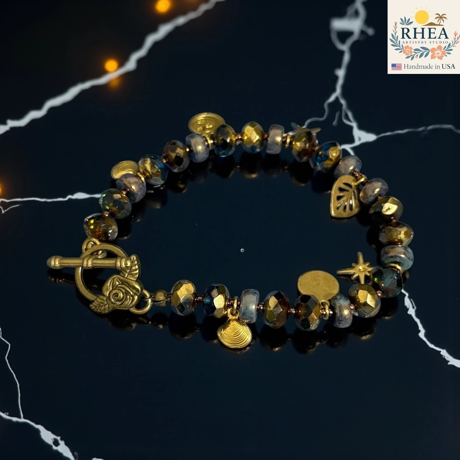Rhea Artistry Studio handmade bracelet with blue and gold glass beads, brass celestial charms, and floral toggle clasp.