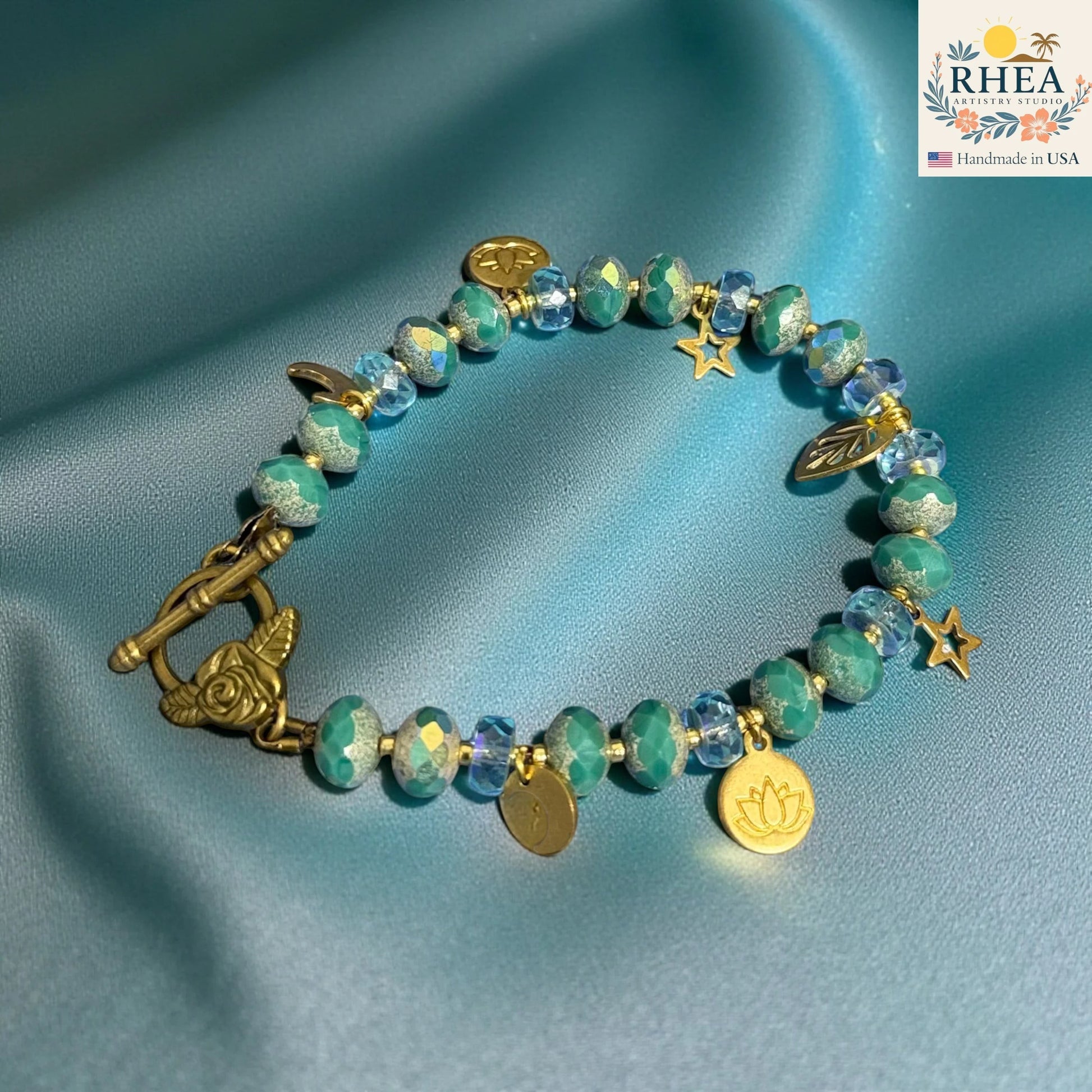Rhea Artistry Studio handmade bracelet with teal and blue glass beads, brass star, moon, and lotus charms, and floral toggle clasp.