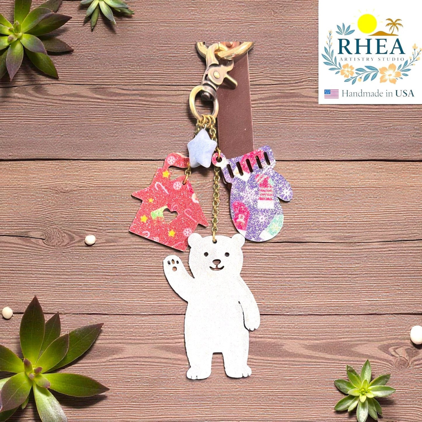 Rhea Artistry Studio handmade leather Christmas charm featuring a white polar bear, red glittery Christmas tree, and purple glittery mitten.