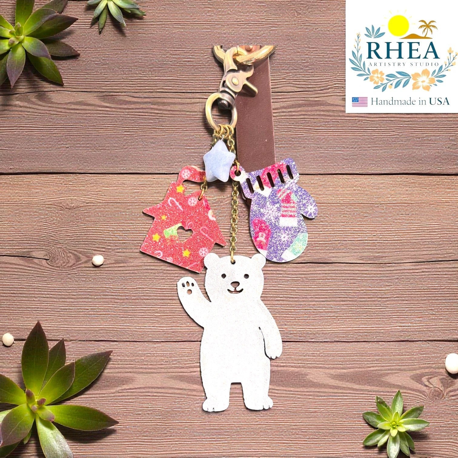 Rhea Artistry Studio handmade leather Christmas charm featuring a white polar bear, red glittery Christmas tree, and purple glittery mitten.