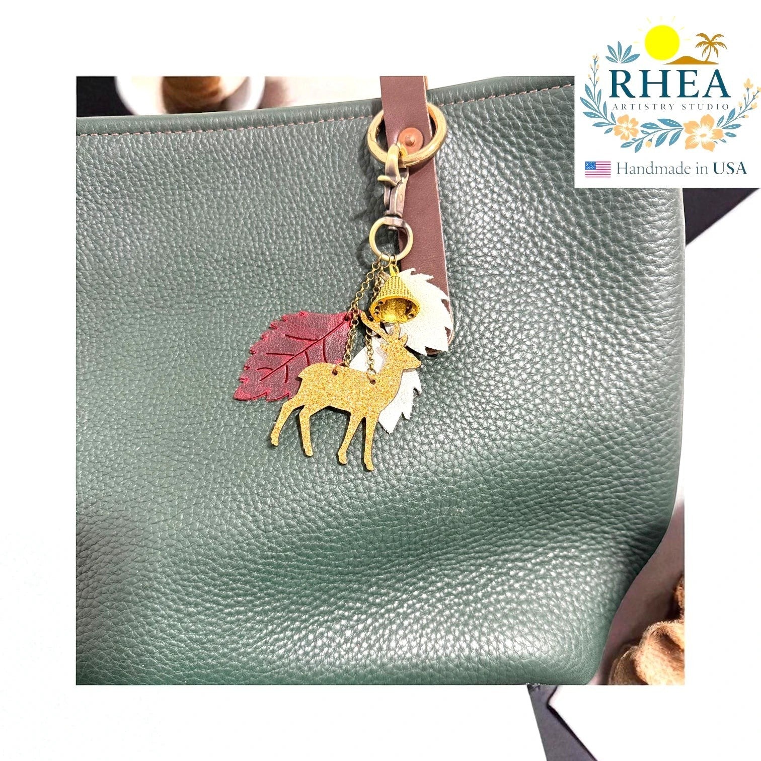 Rhea Artistry Studio handmade leather Christmas charm with gold glitter deer, red leaf, white leaf, and bell on a green pebbled leather bag.