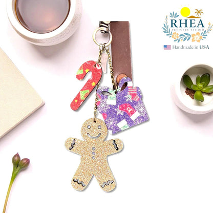 Rhea Artistry Studio Christmas Tales leather charm set with gingerbread man, candy cane, and gift box designs. Glitter and matte finishes with brass hardware.