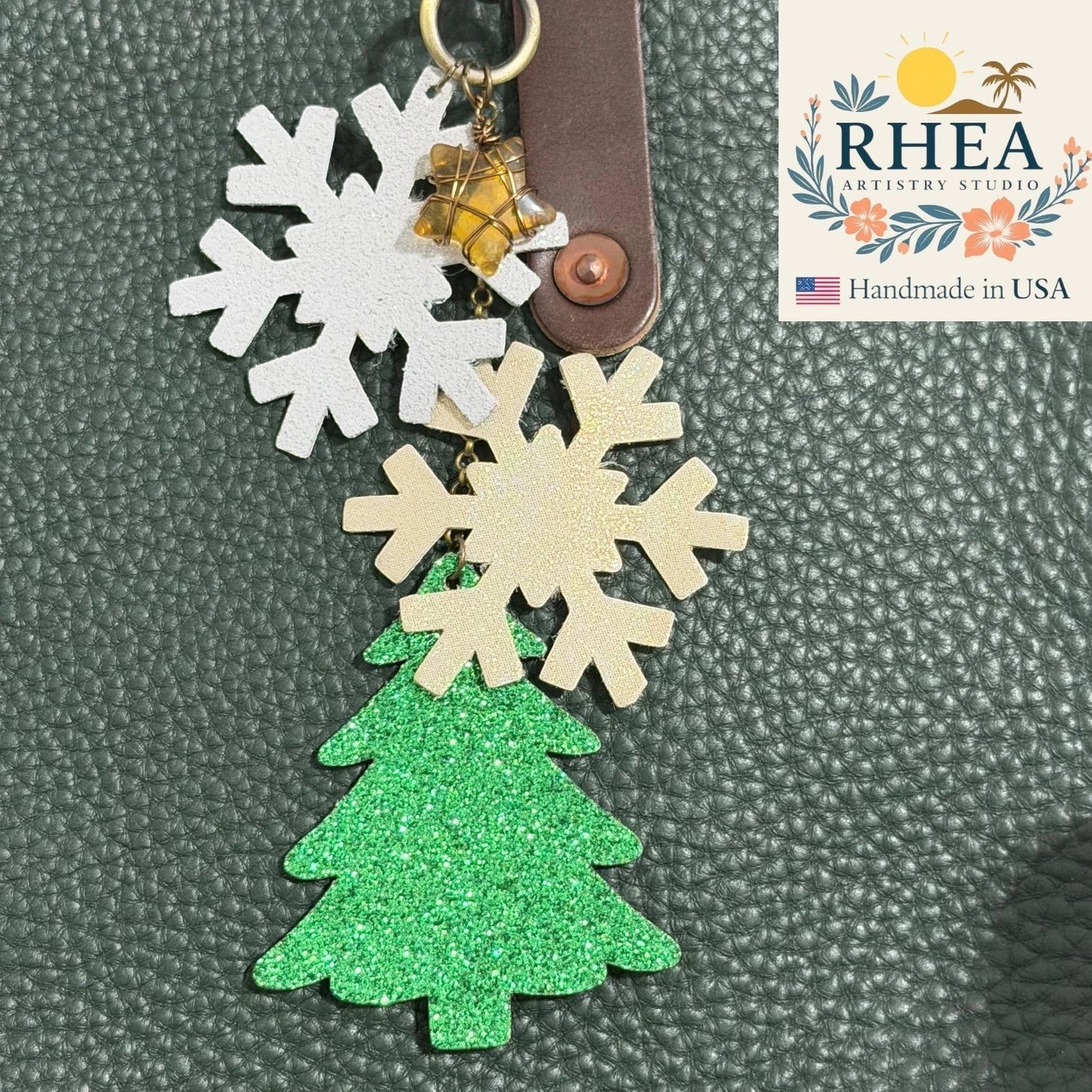 Rhea Artistry Studio handmade Christmas leather charm with white and gold glitter snowflakes, green glitter Christmas tree, and citrine star accent.