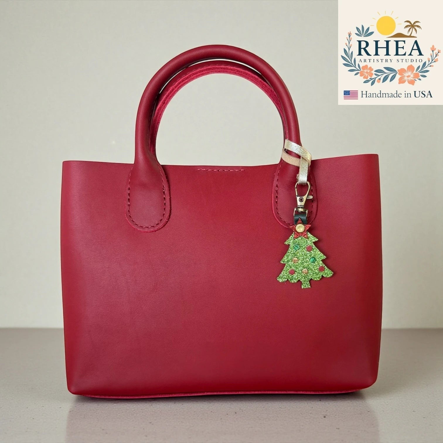 Rhea Artistry Studio red leather handbag with a glittery green Christmas tree charm attached to the handle.