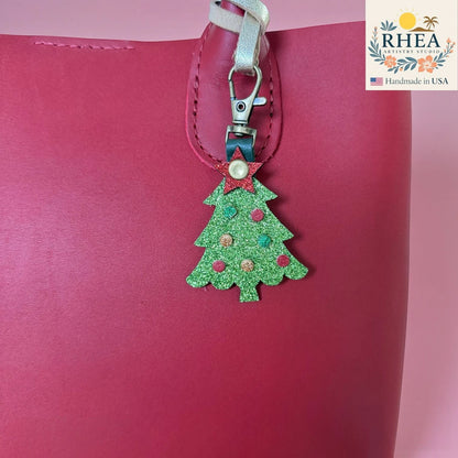 Rhea Artistry Studio green glitter Christmas tree charm with red and gold ornaments and a red star topper, attached to a red bag.