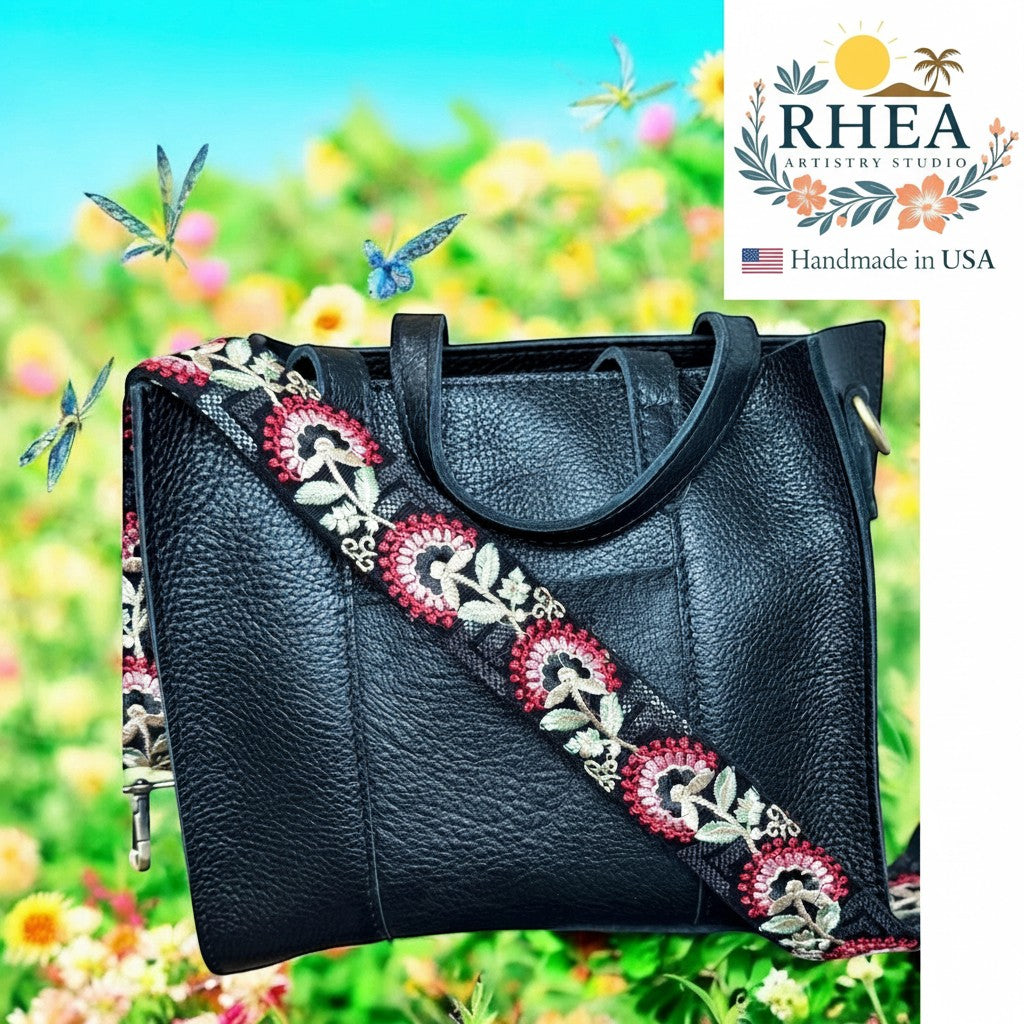 Rhea Artistry Studio black leather handbag with a 2-inch wide crimson tapestry embroidered strap featuring floral motifs. Adjustable strap with brushed brass hardware.