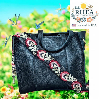 Rhea Artistry Studio black leather handbag with a 2-inch wide crimson tapestry embroidered strap featuring floral motifs. Adjustable strap with brushed brass hardware.