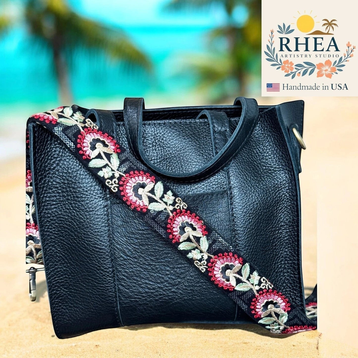 Rhea Artistry Studio black leather tote with a 2-inch wide crimson tapestry embroidered strap featuring floral motifs. Adjustable crossbody strap.