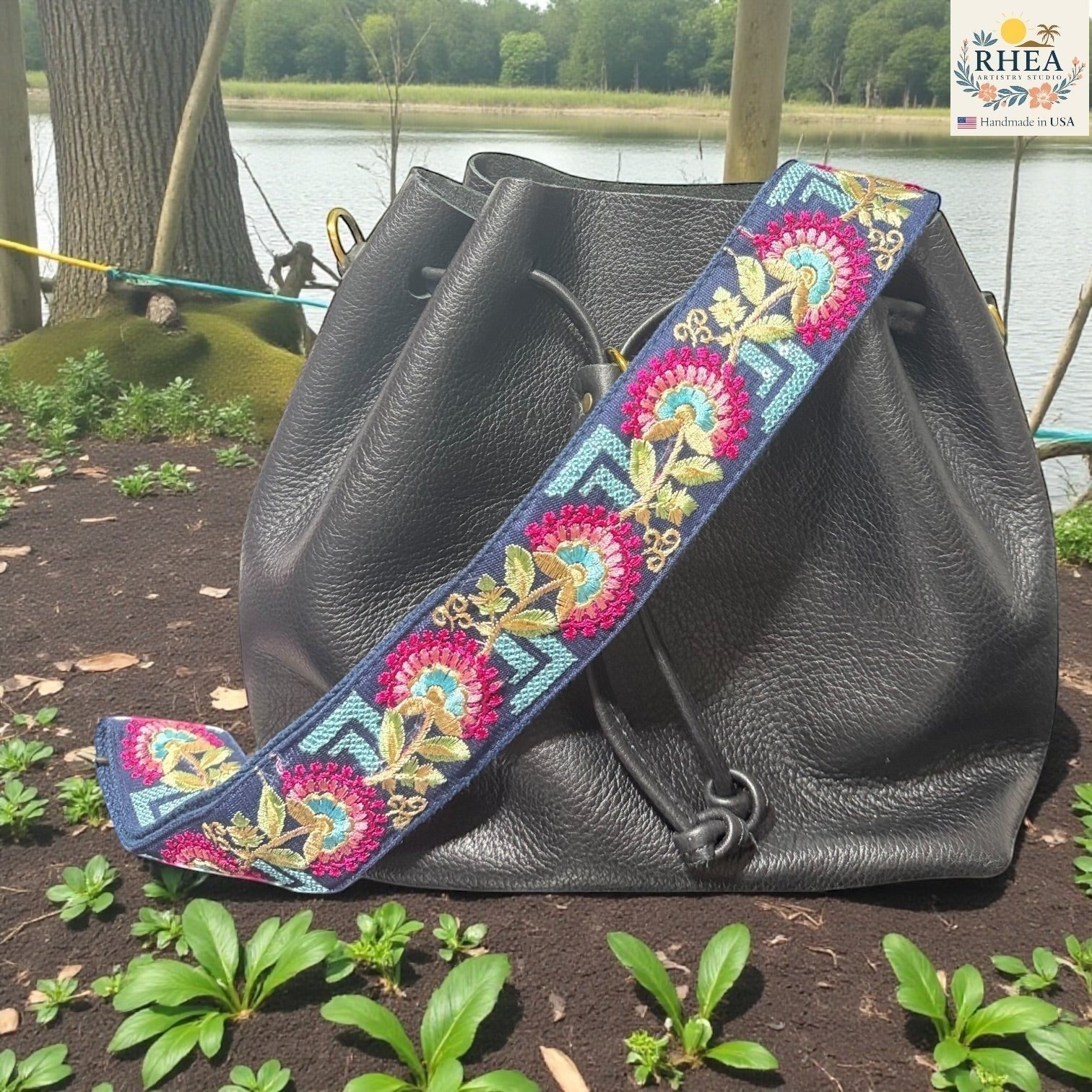 Rhea Artistry Studio navy blue crossbody strap with embroidered floral motifs in pink, teal, and gold. Adjustable 2-inch width.