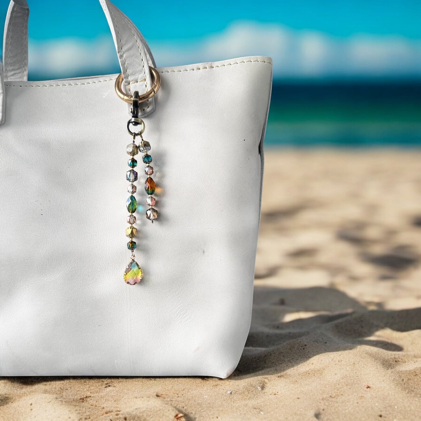 Rhea Artistry Studio elegant crystal beaded keychain with teardrop pendant and brass accents on a white tote bag at the beach.