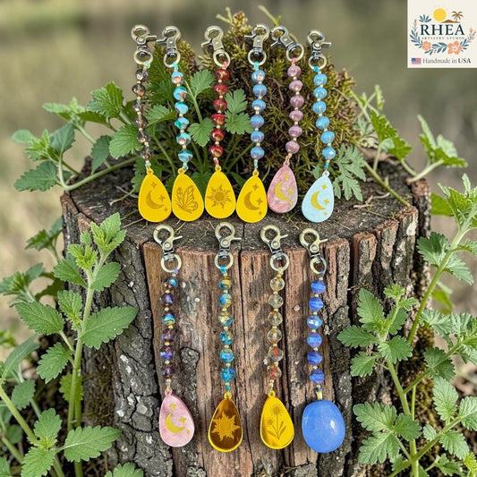 Rhea Artistry Studio artisan bag charms with Czech glass beads, brass accents, and hand-painted pendants featuring celestial and nature motifs.