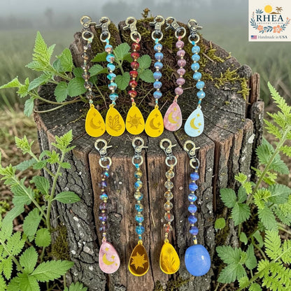 Rhea Artistry Studio artisan bag charms with Czech glass beads, brass accents, and hand-painted pendants featuring celestial and nature motifs.