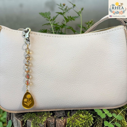 Rhea Artistry Studio artisan bag charm with Czech glass beads, brass accents, and a hand-painted yellow pendant featuring two flowers.