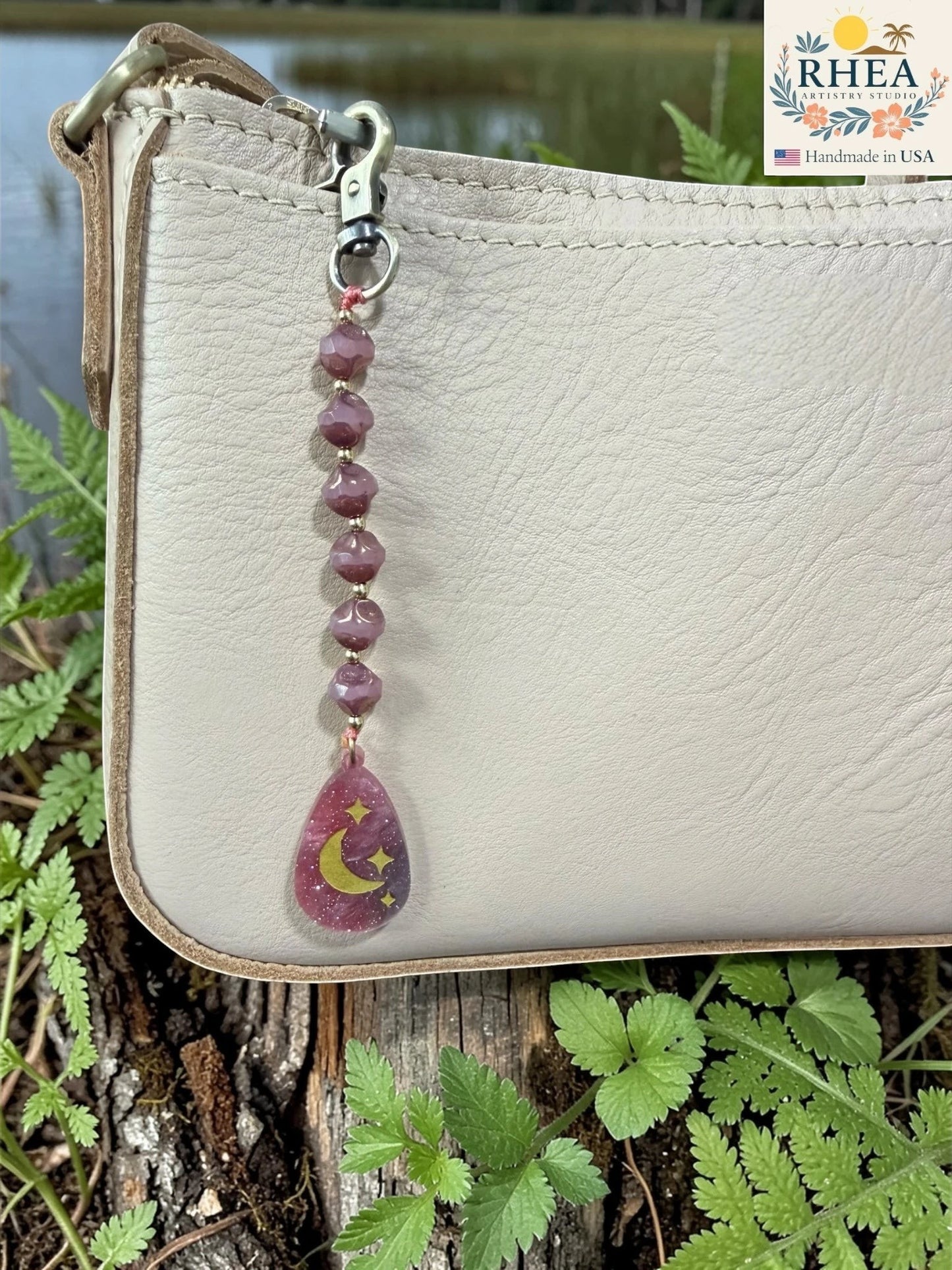 Rhea Artistry Studio artisan bag charm with purple Czech glass beads and a hand-painted pendant featuring a crescent moon and stars.
