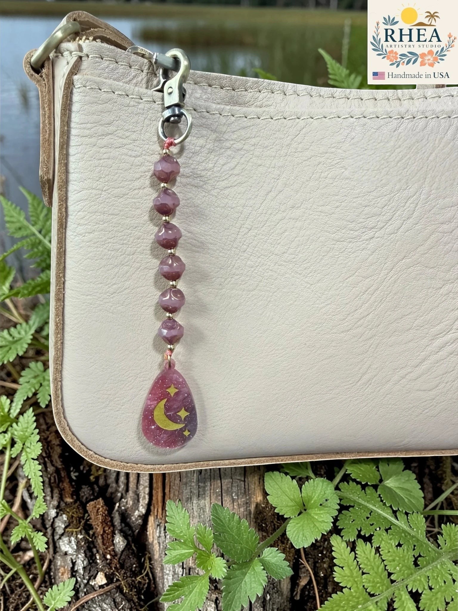 Rhea Artistry Studio artisan bag charm with purple Czech glass beads and a hand-painted pendant featuring a crescent moon and stars.