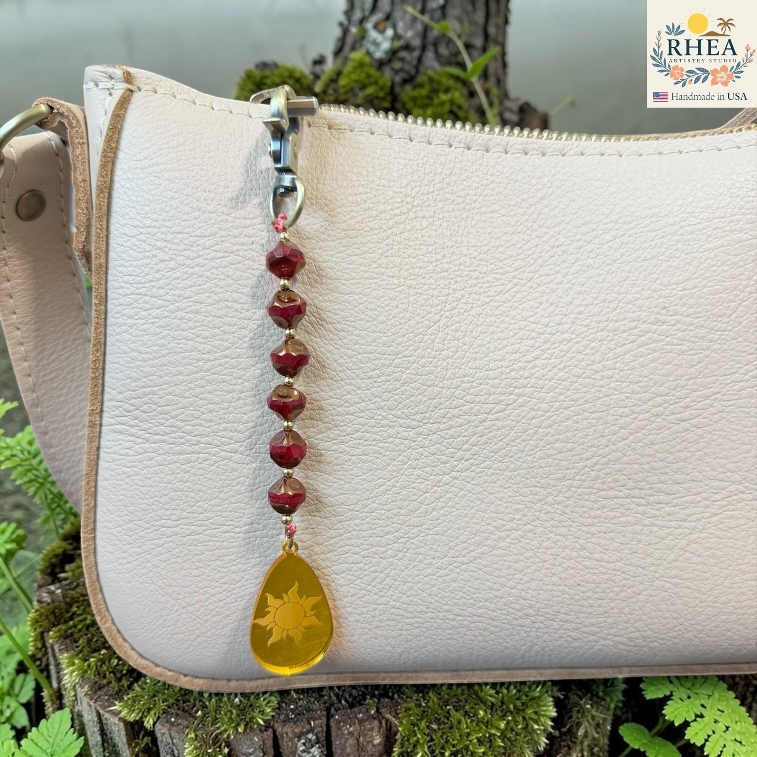 Rhea Artistry Studio artisan bag charm with red Czech glass beads, brass accents, and a yellow hand-painted sun pendant.